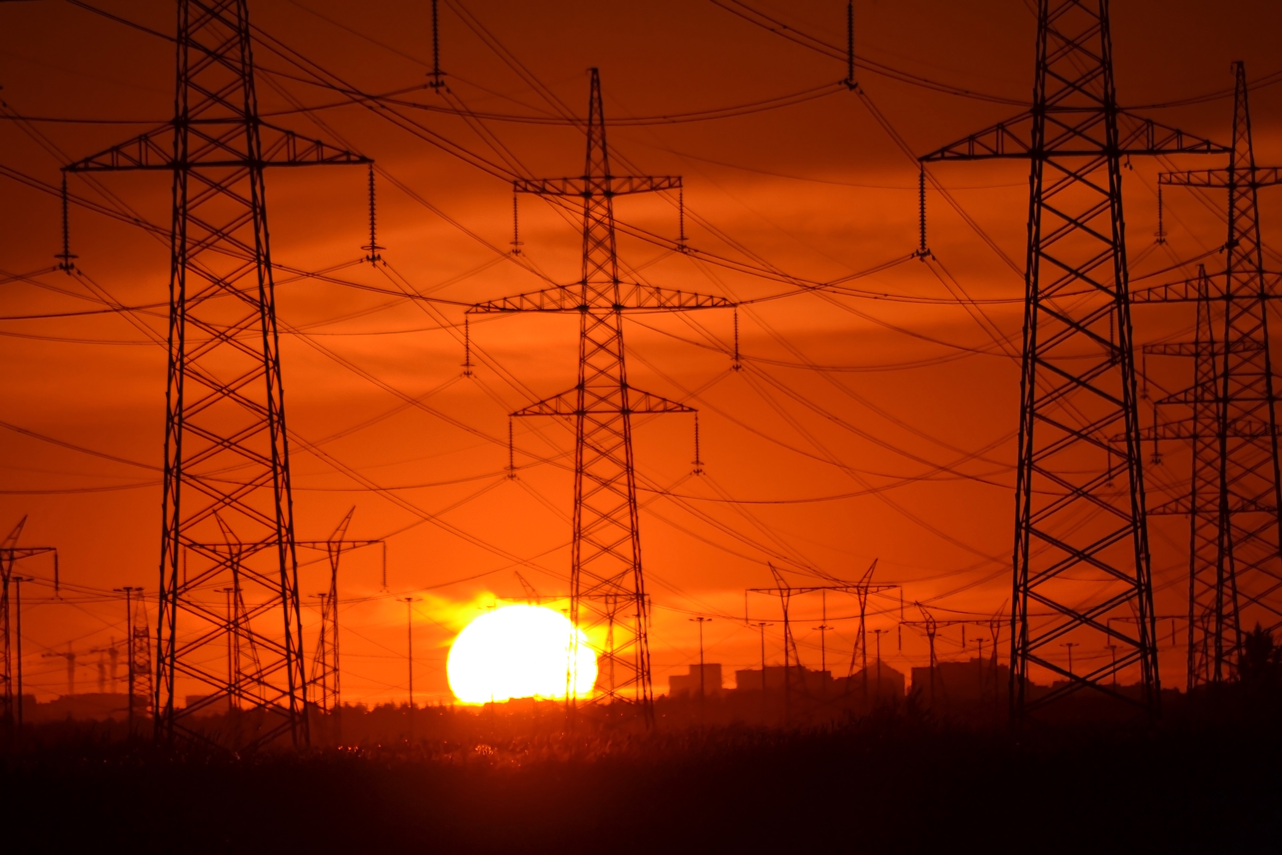 Torres de alta tensión en silueta al atardecer con cielo naranja intenso, representando la infraestructura de transporte eléctrico en España