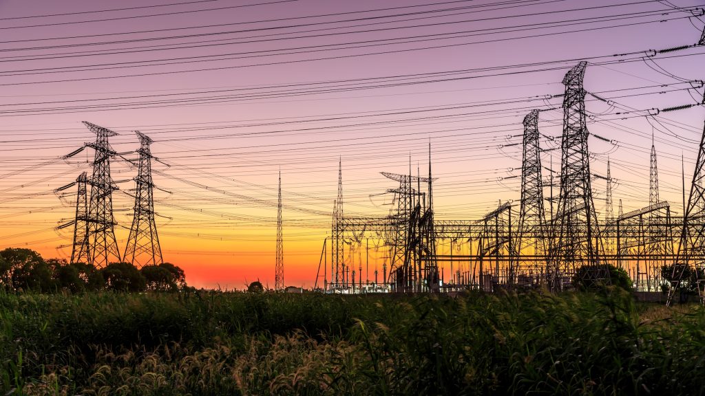 Subestación eléctrica con torres de alta tensión en silueta al atardecer, representando la infraestructura de red y los mecanismos de equilibrio del sistema eléctrico