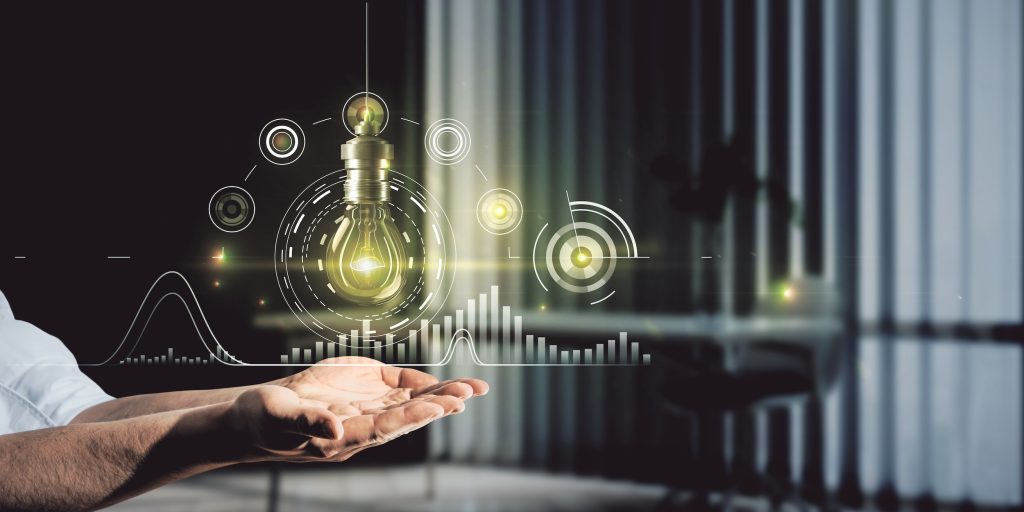Mano sosteniendo una bombilla con gráficas y datos energéticos proyectados, representando la integración de tecnología y análisis en la gestión del mercado eléctrico