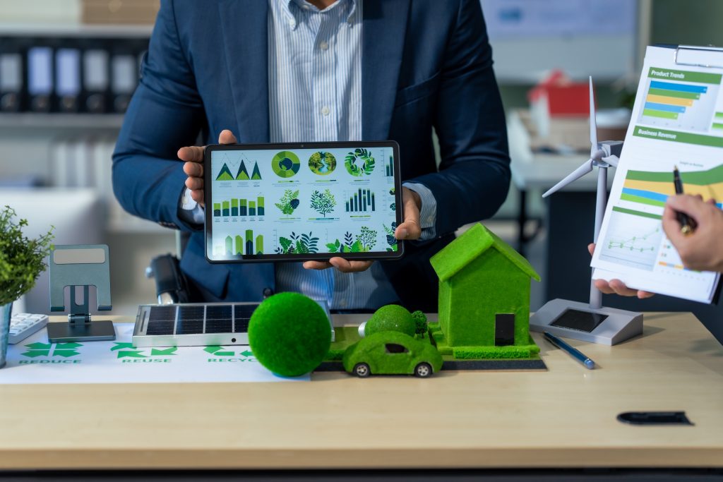 Profesional presentando análisis de energía renovable con tablet y maquetas de aerogeneradores y paneles solares